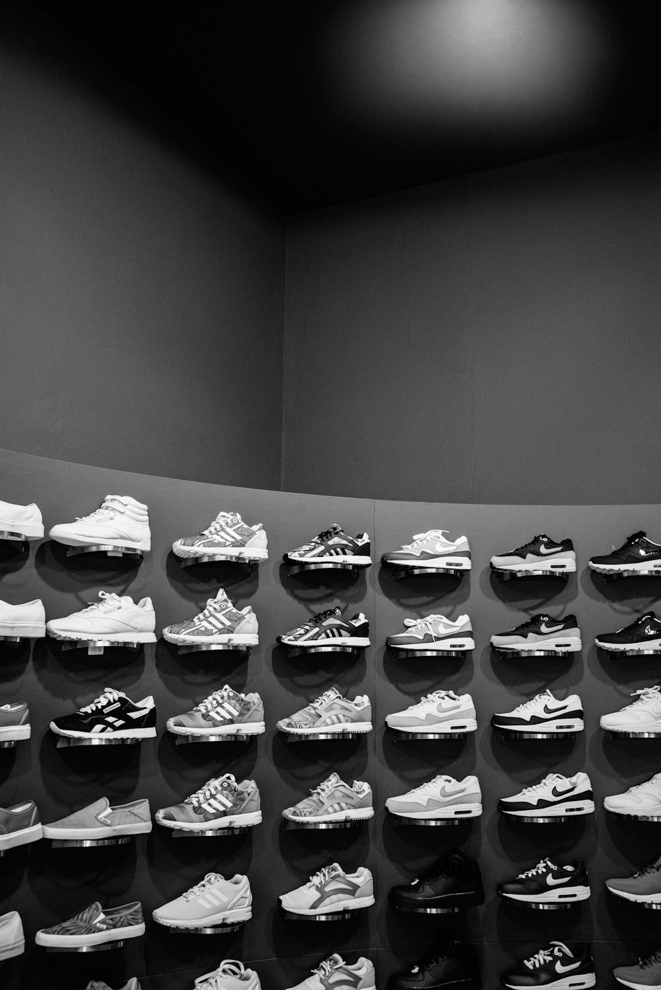 Athletic sneakers displayed on shelves against a grey wall.