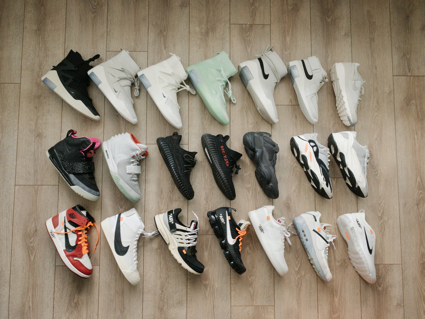 Rows of assorted designer sneakers arranged on a wooden floor.