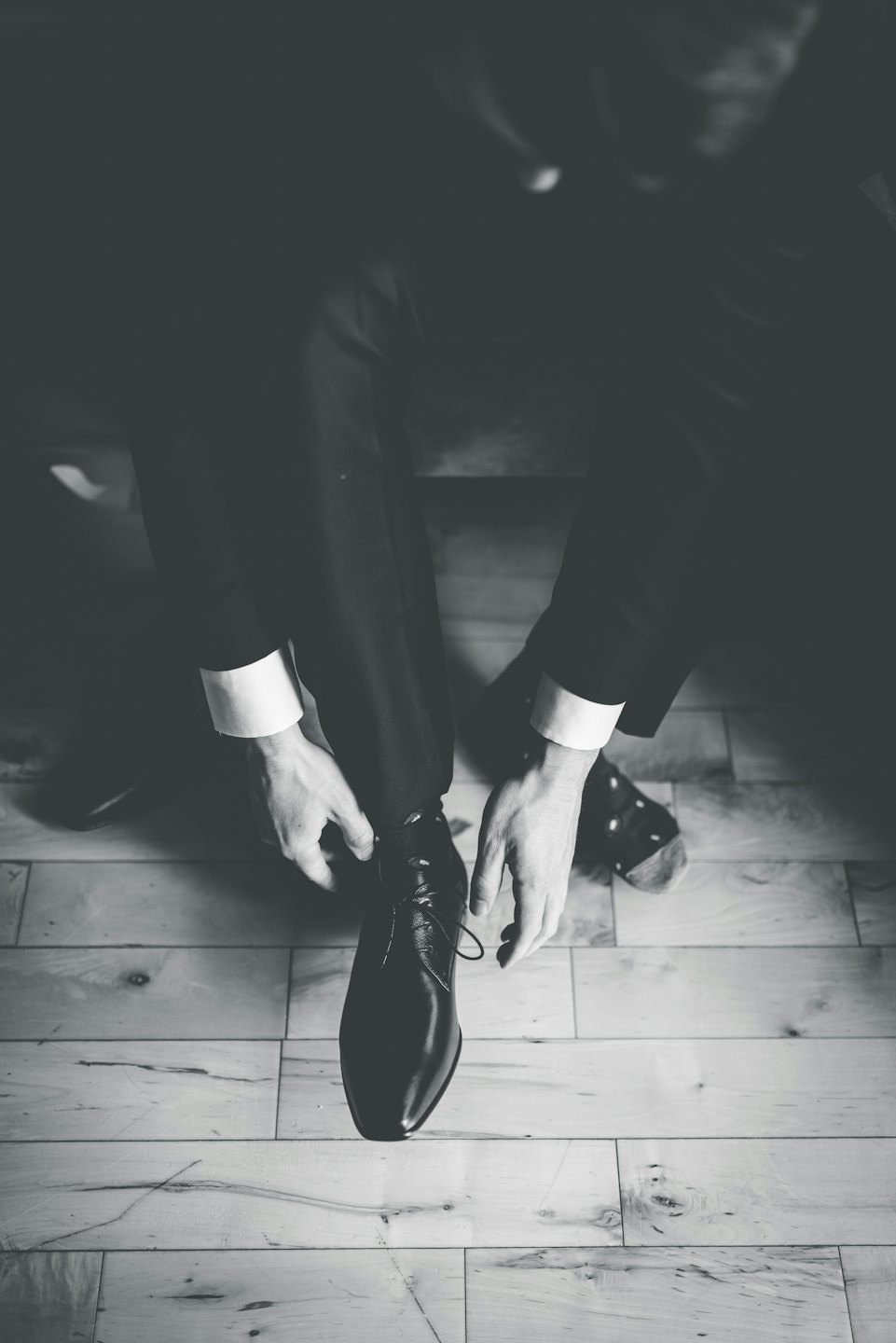 A man tying his black leather dress shoe.